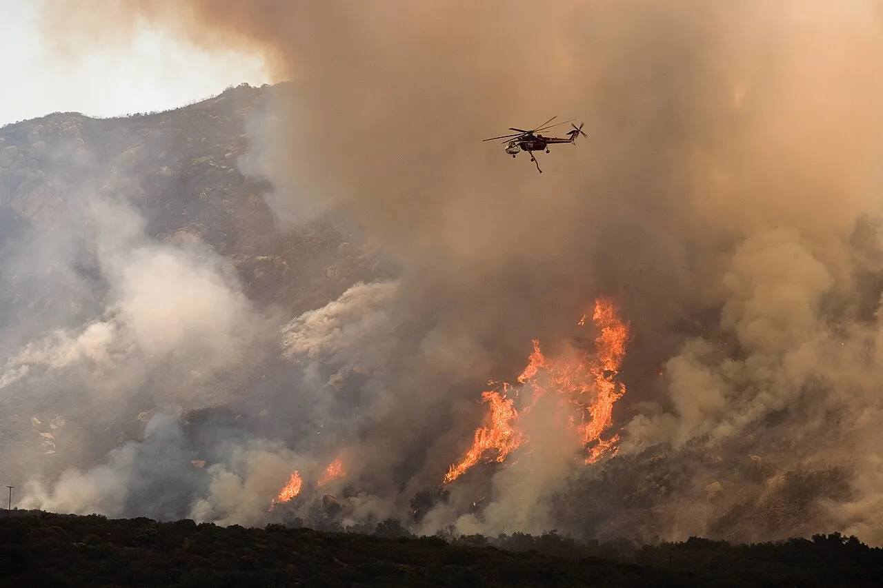 A helicopter flies above a burning hillside in California